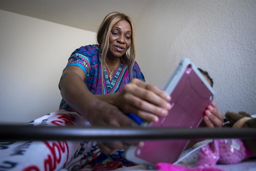 JaReen Williams adjusts an iPad for her sixteen year old daughter, Lydia, as Lydia navigates to one of her comfort shows, Charlie Brown, in preparation for her triweekly treatment by a nurse on Friday, April 12, 2024, in Katy.