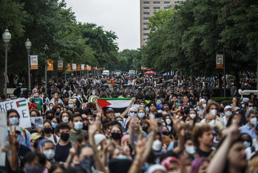 A crowd of protesting students march down Speedway at The University of Texas at Austin on April 24, 2024. State police officers march behind them.