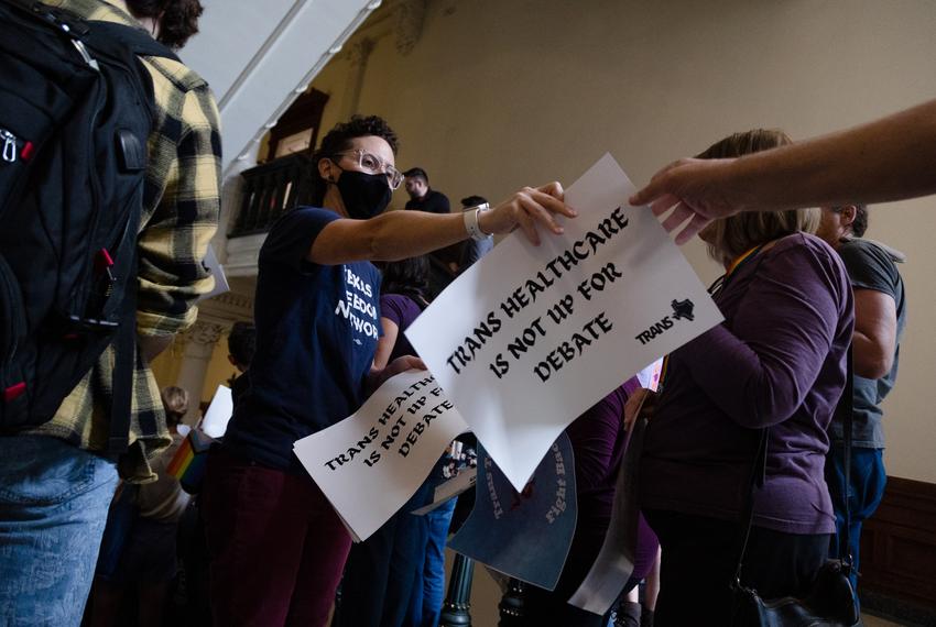 Marti Bier with Texas Freedom Network passes out signs that read "Trans healthcare is not up for debate" before a press conference on the stairs across from the House floor to protest SB 14, which seeks to ban puberty blockers and hormone therapies for transgender youth, at the state Capitol in Austin on May 12, 2023.