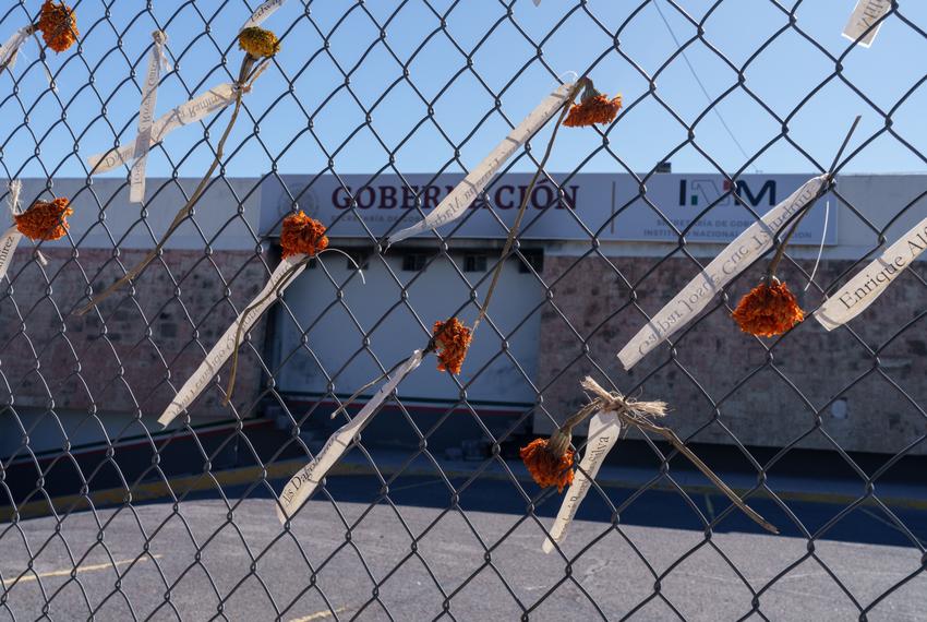 Strips of paper bearing the names of the 40 men killed in the fire are tied with marigolds to the fence surrounding the immigration detention center where they died.