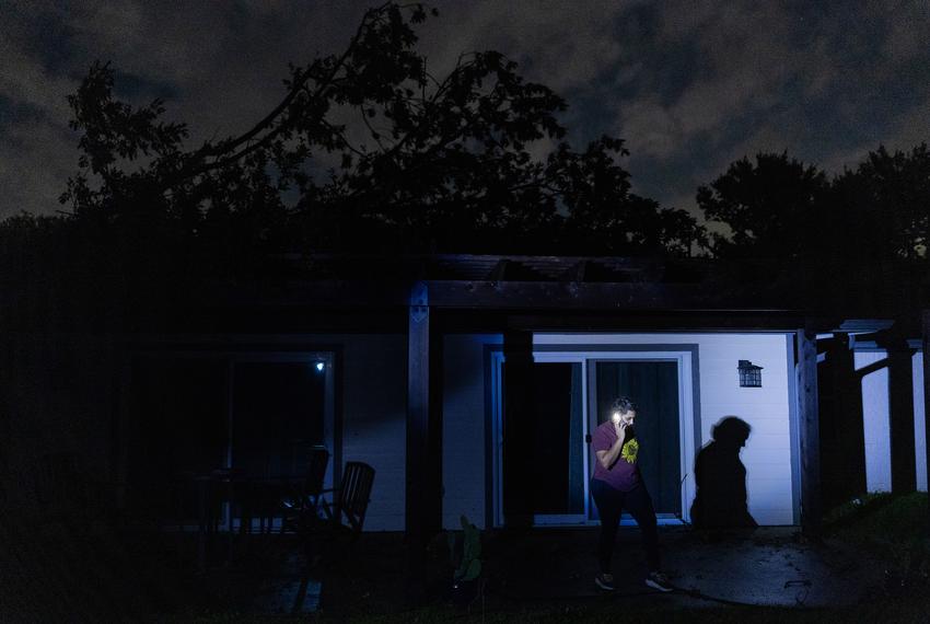 Anastasia Gill, 38, takes a call in the darkness of her backyard after losing electricity on May 16, 2024, in Houston. The roof of her house sustained damages after a tree fell on it during the storm on Thursday. (Marie D. De Jesús / Houston Landing)