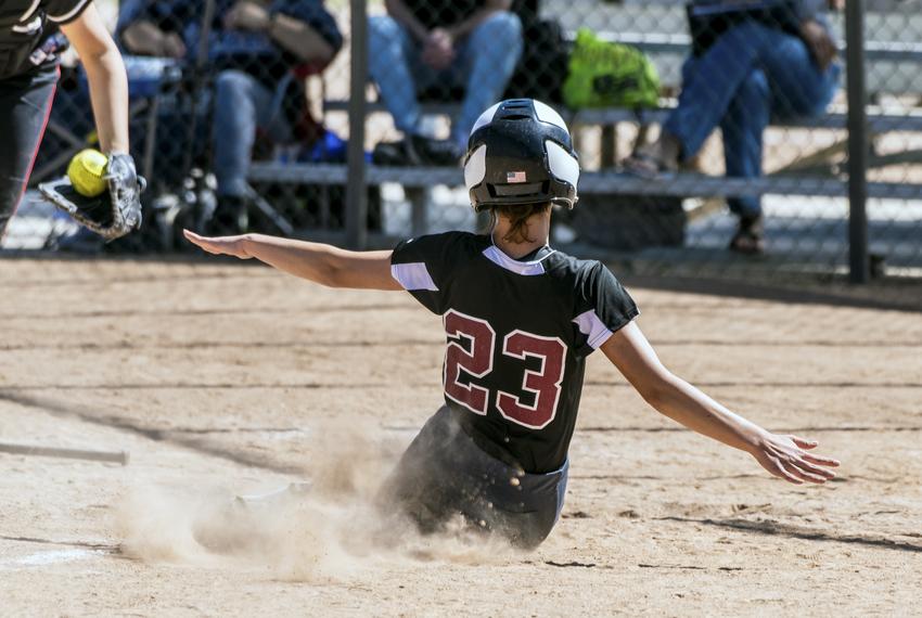 A teenage softball player in black uniform slides into home plate.