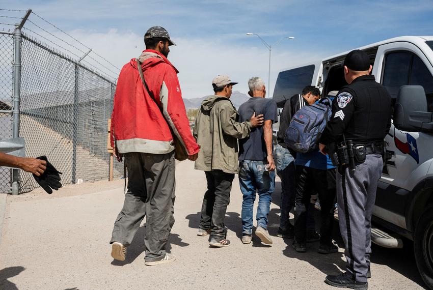 A group of migrants walk to an El Paso County Sheriff transport van to be taken to processing on March 20, 2024.