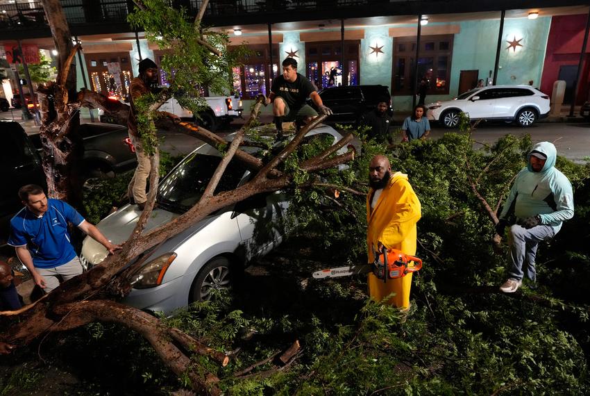 Rapper Trae tha Truth, in yellow, cuts fallen tree limbs on top of a car in the aftermath of a severe thunderstorm that passed through downtown Houston on May 16, 2024.