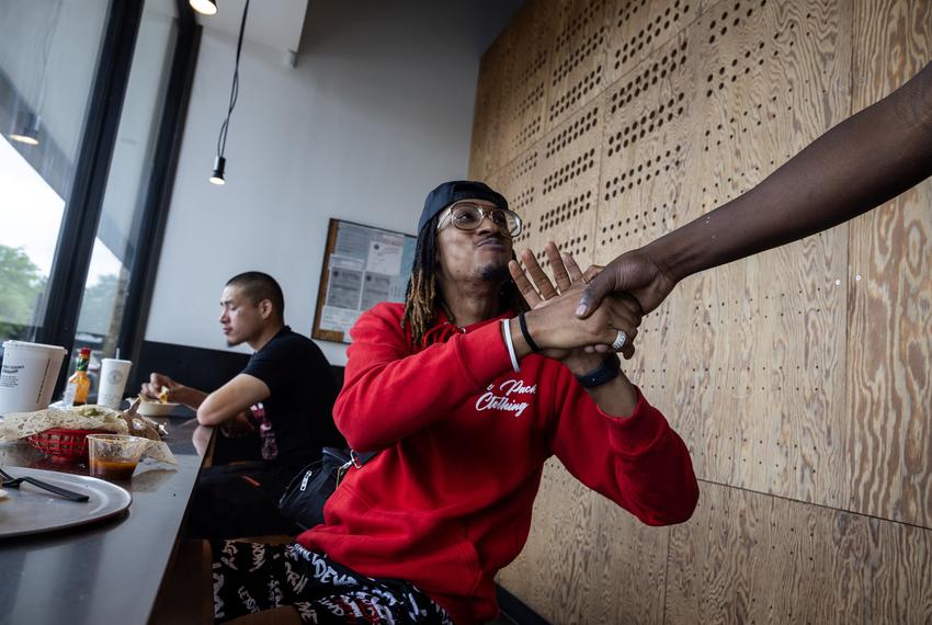 Prince Hayward, a traditional support specialist at University of Houston’s Charge Up program, at center, says hello to a friend while grabbing lunch with “Spider,” at left, a young adult he is mentoring, on April 26 at Chipotle Mexican Grill in Houston.