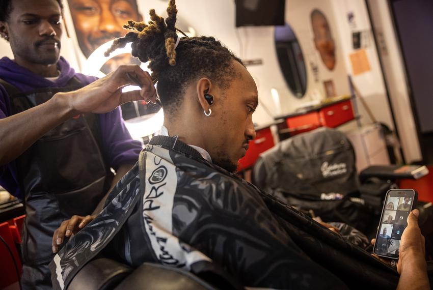 Prince Hayward, a traditional support specialist at the University of Houston’s Charge Up program, takes a meeting while getting a haircut by Walter White III on April 18 in Houston.